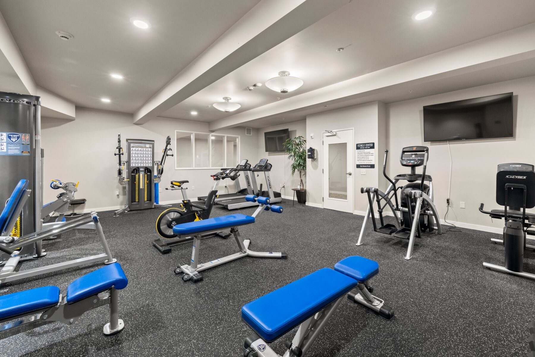 fitness center with strength machines, cardio machines, and mounted televisions