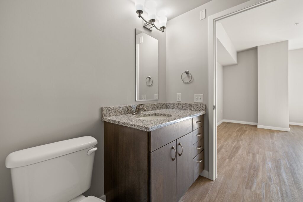 bathroom with granite countertops, wall mirror, single sink, wood-style flooring, and access to bedroom
