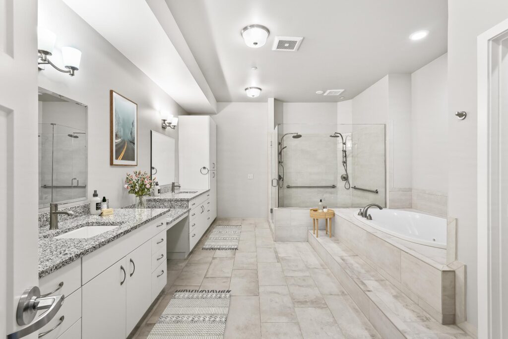 large bathroom with double sink, recessed tub, and glass shower stall