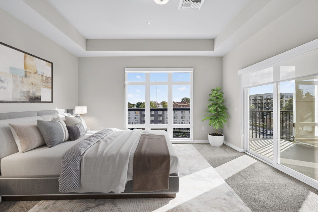 A modern, bright bedroom with a large bed, neutral bedding, abstract wall art, and a potted plant. Sunlight streams through large windows and a glass door that opens to a balcony with city views.