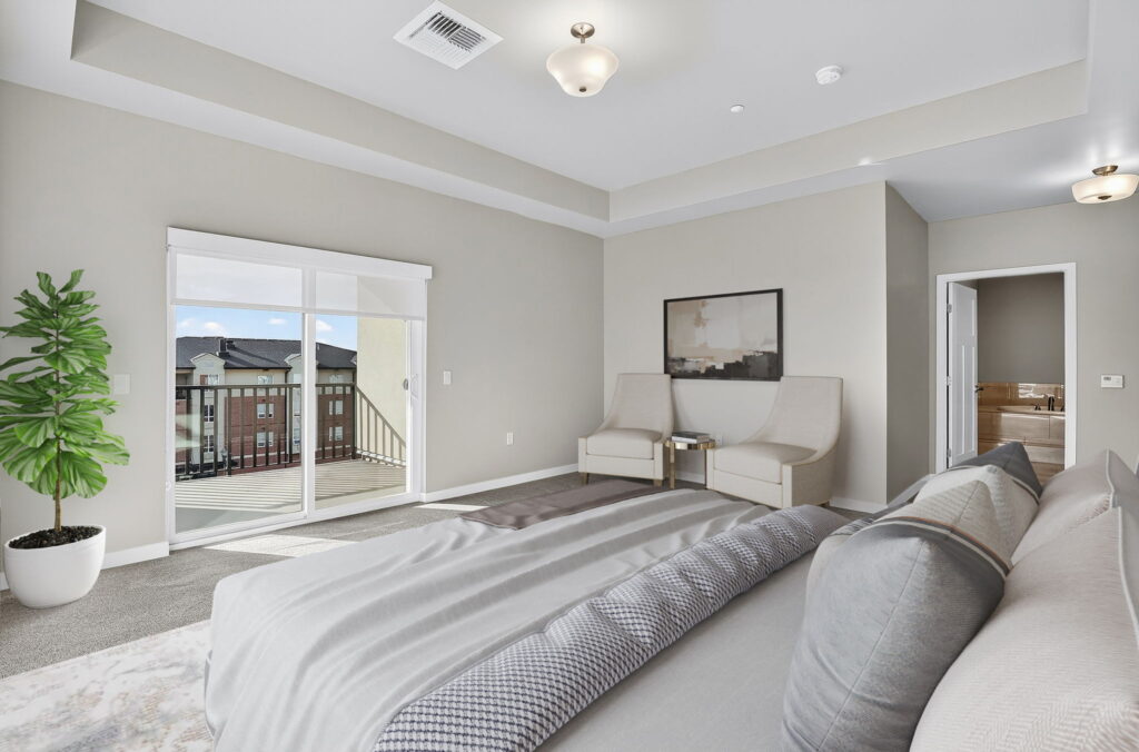 A modern bedroom with a large bed, two beige chairs, a potted plant, a painting on the wall, light gray walls, and a sliding glass door leading to a balcony with a view of neighboring buildings.
